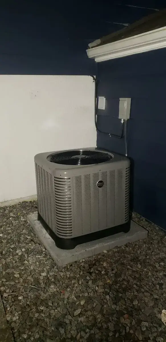 Outdoor heat pump or AC unit on a concrete pad with a wall-mounted disconnect
